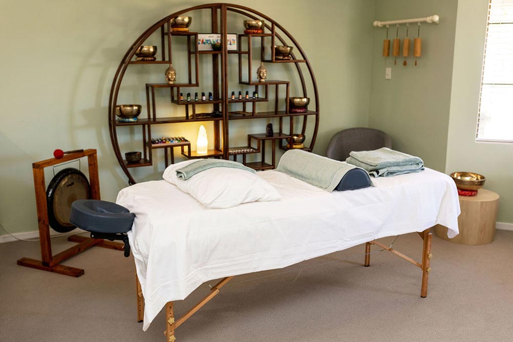 Bowen Therapy room with massage table, sound therapy gong and bowls, wind chimes, and a large round display unit
